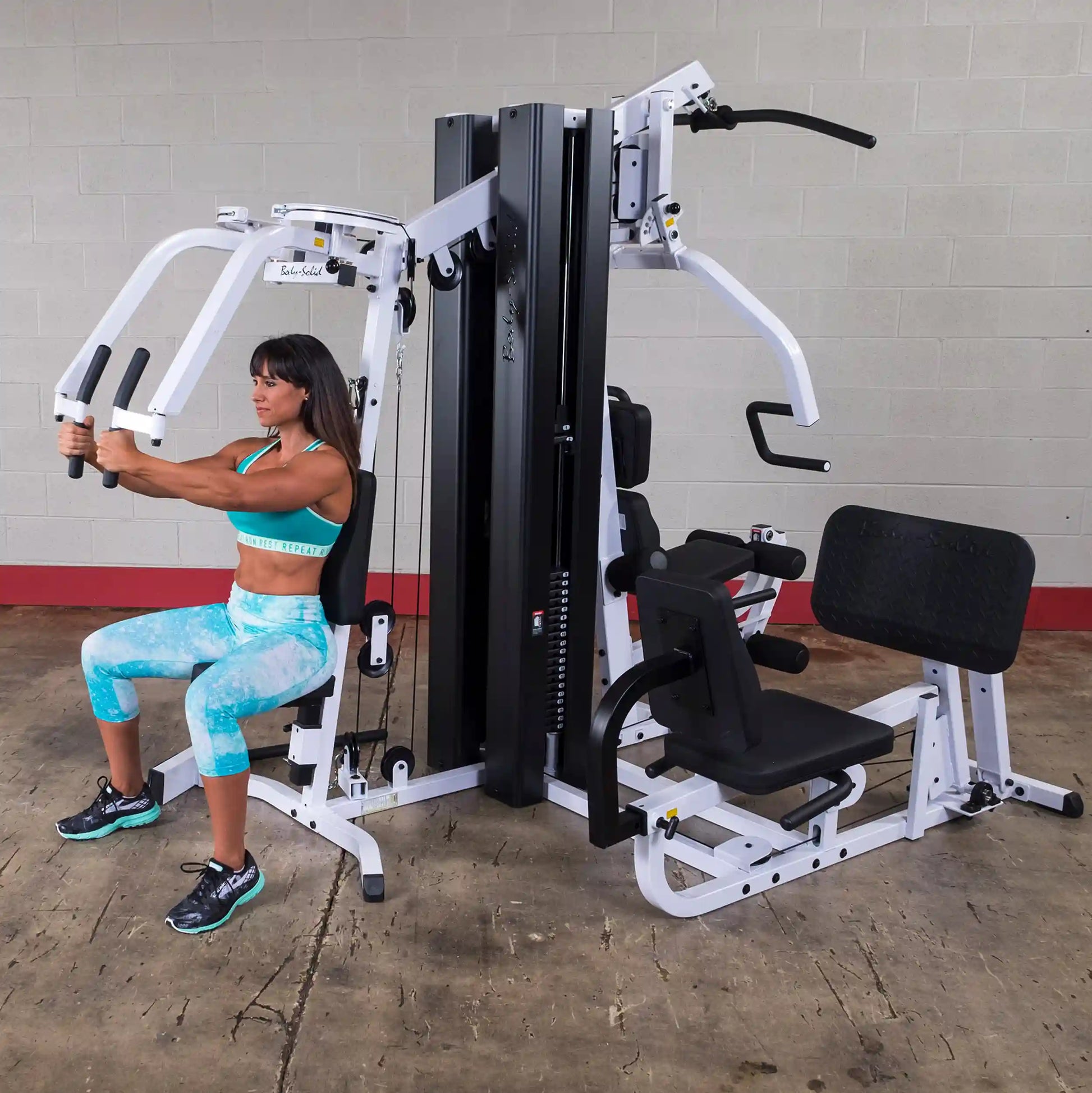 Woman using Body-Solid home gym with white frame for strength training.