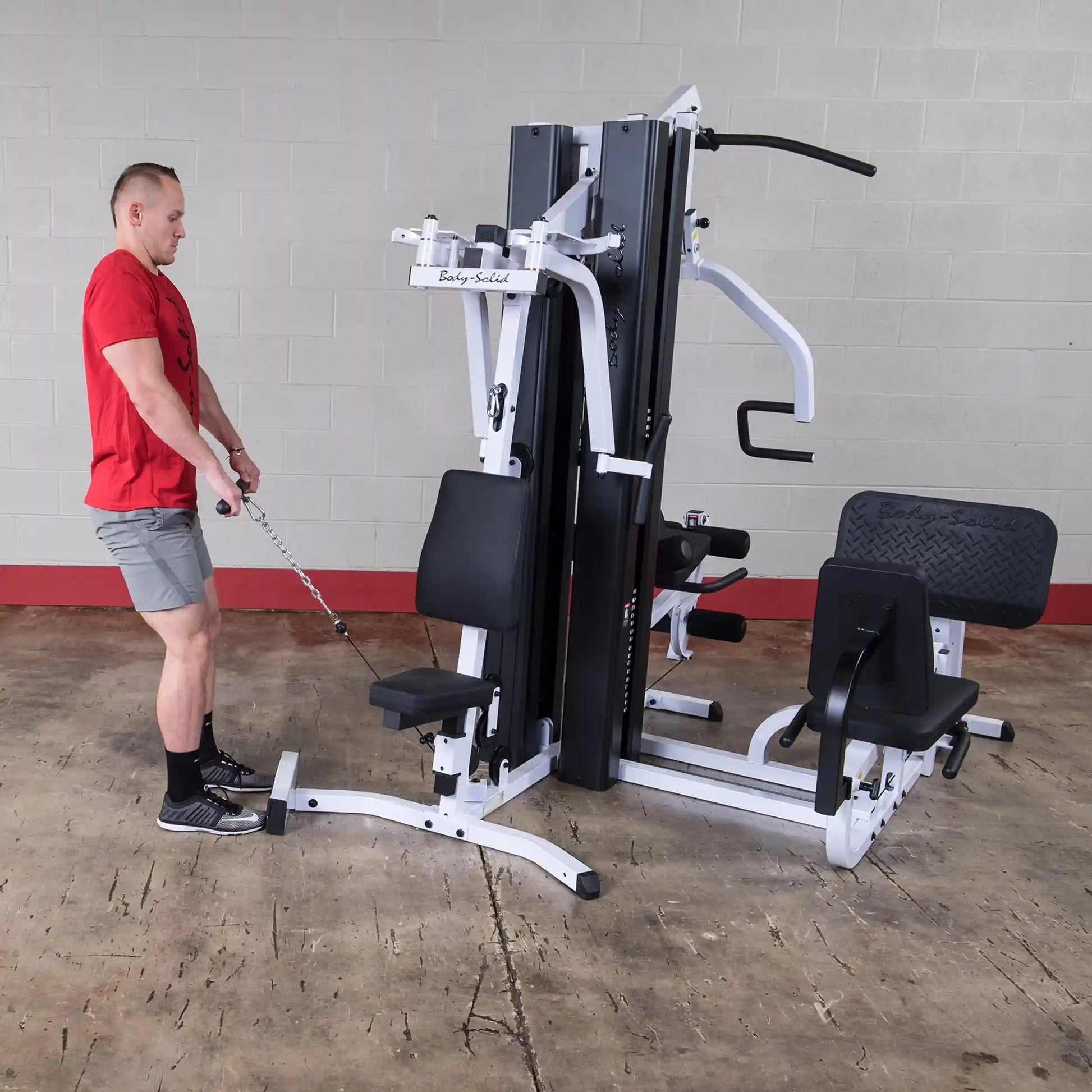 Man using Body-Solid home gym machine in a red shirt and gray shorts.