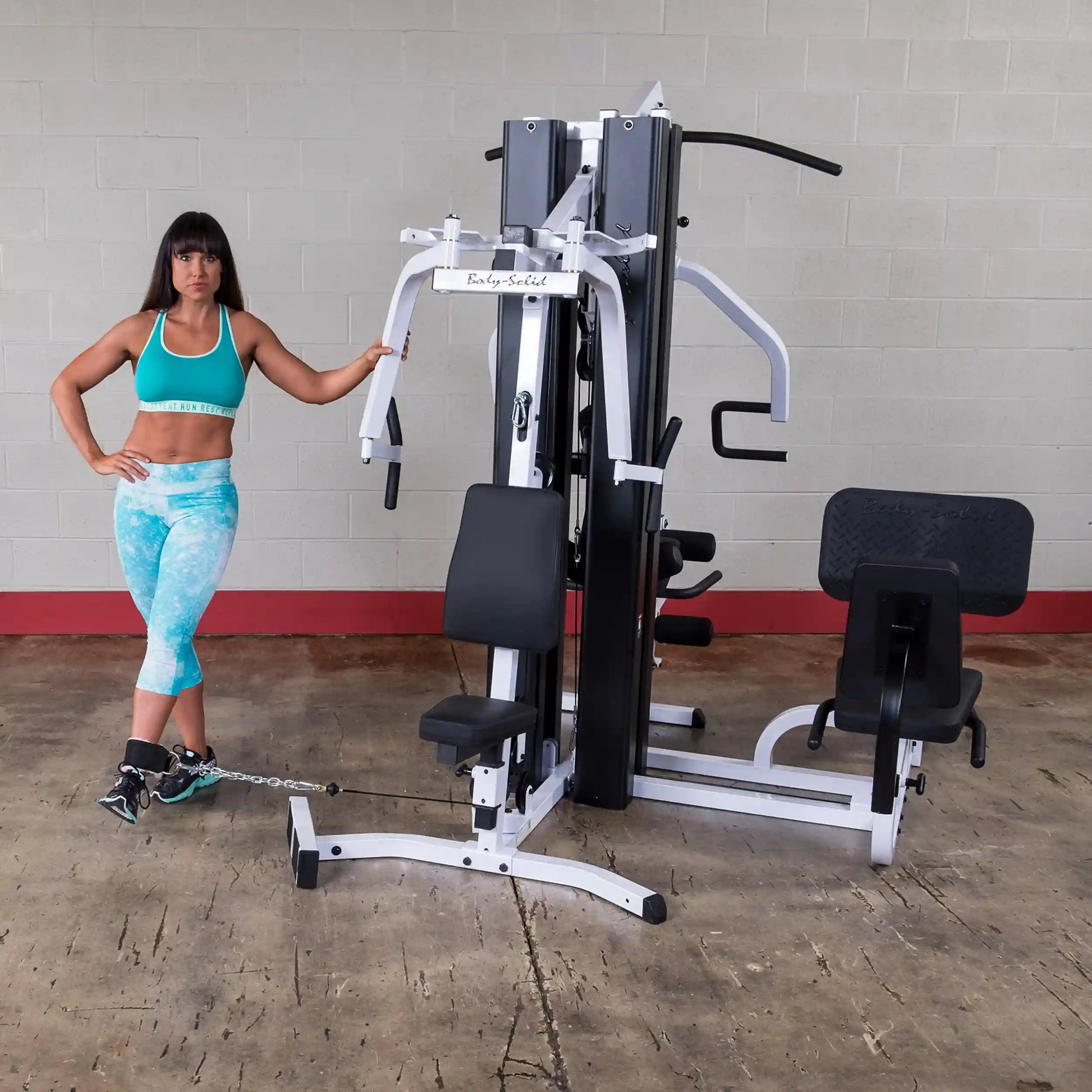 Woman in teal workout gear using Body-Solid home gym with leg extension attachment.