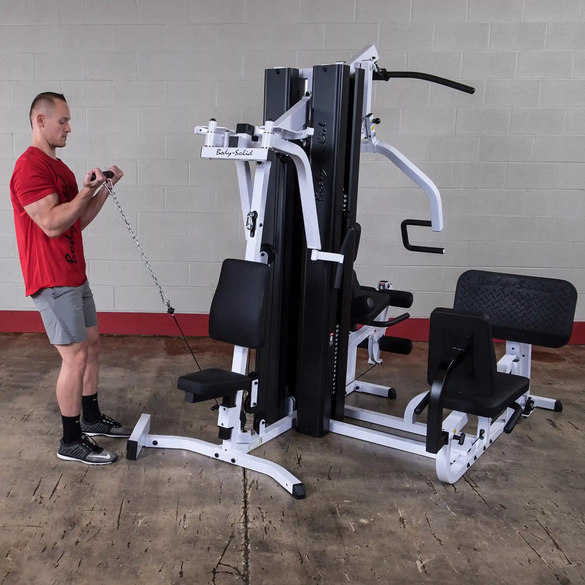 Man using Body-Solid multi-station gym equipment with cable attachment in a red shirt.