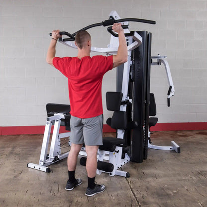 Man using home gym machine in red shirt and gray shorts for upper body workout.