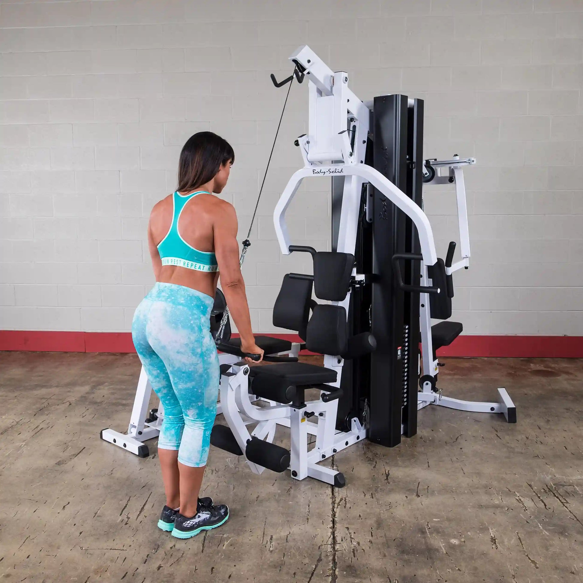 Woman using Body-Solid multi-station gym equipment in turquoise workout attire.