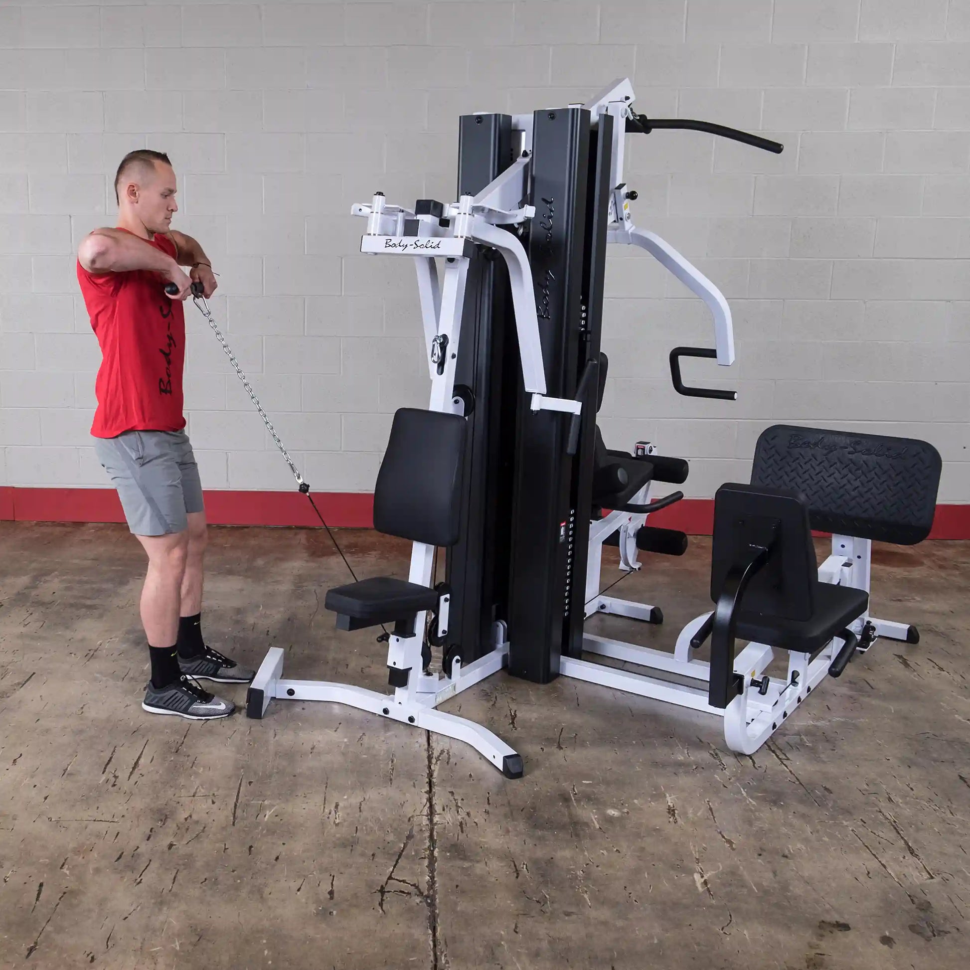 Man using Body-Solid multi-station gym machine in red shirt and gray shorts.