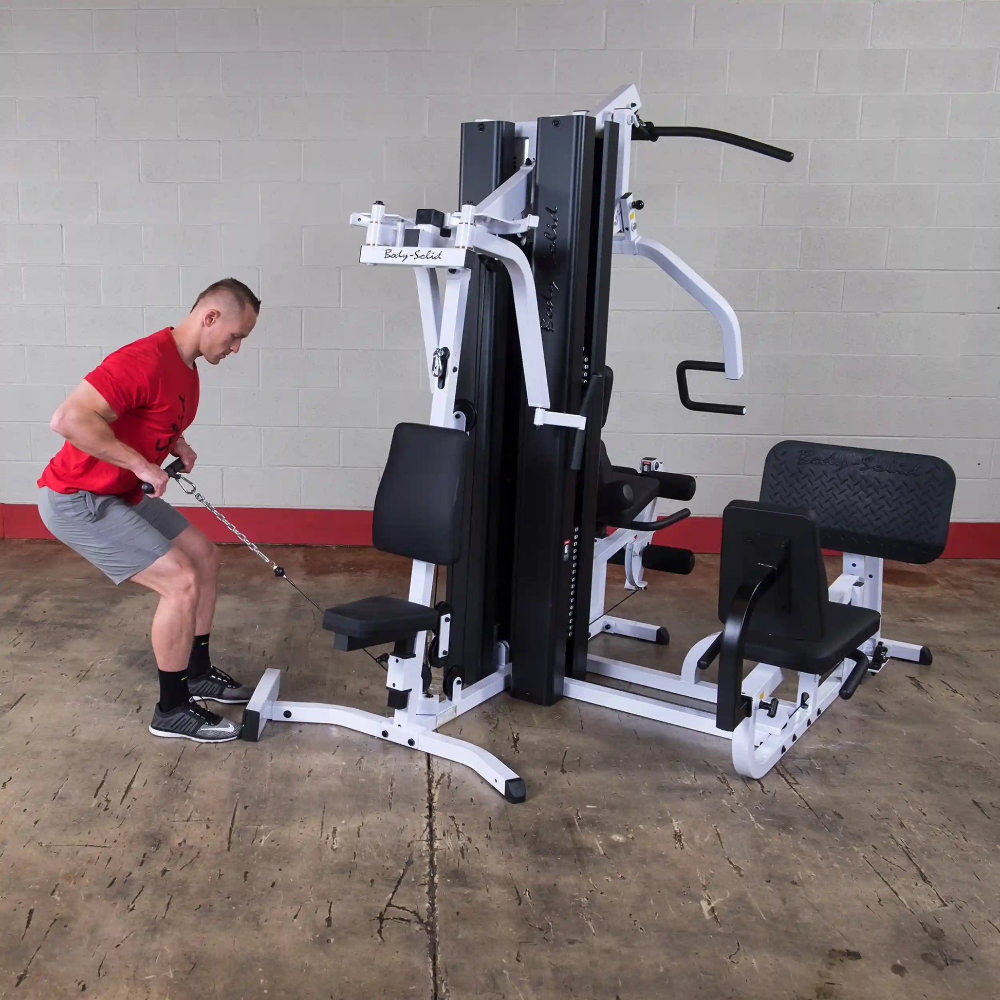 Man using Body-Solid home gym for cable row exercise in red shirt and gray shorts.