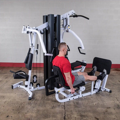 Man in red shirt using a Body-Solid multi-station gym machine for leg presses.