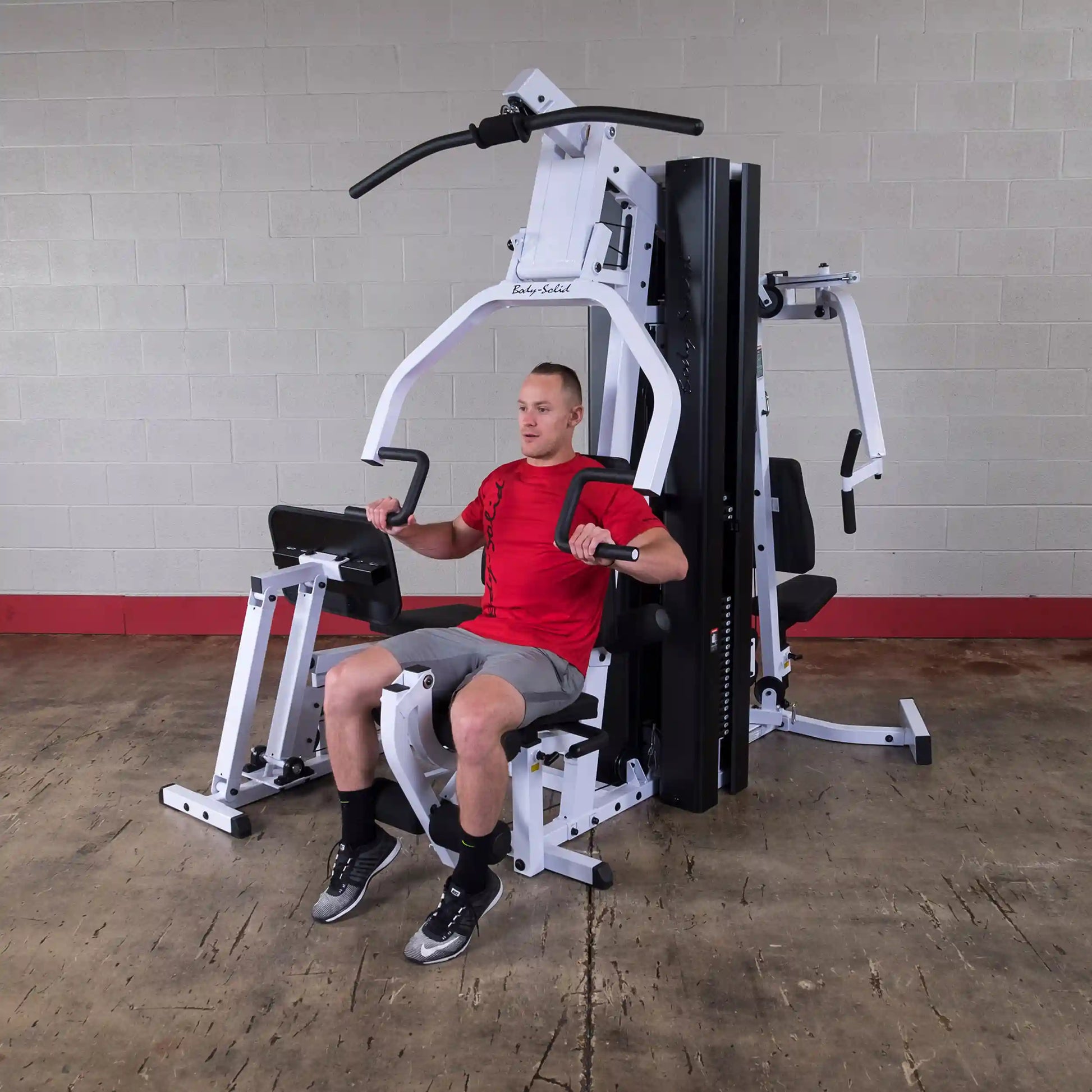 Man using Body-Solid gym equipment in red shirt, performing a strength training exercise.
