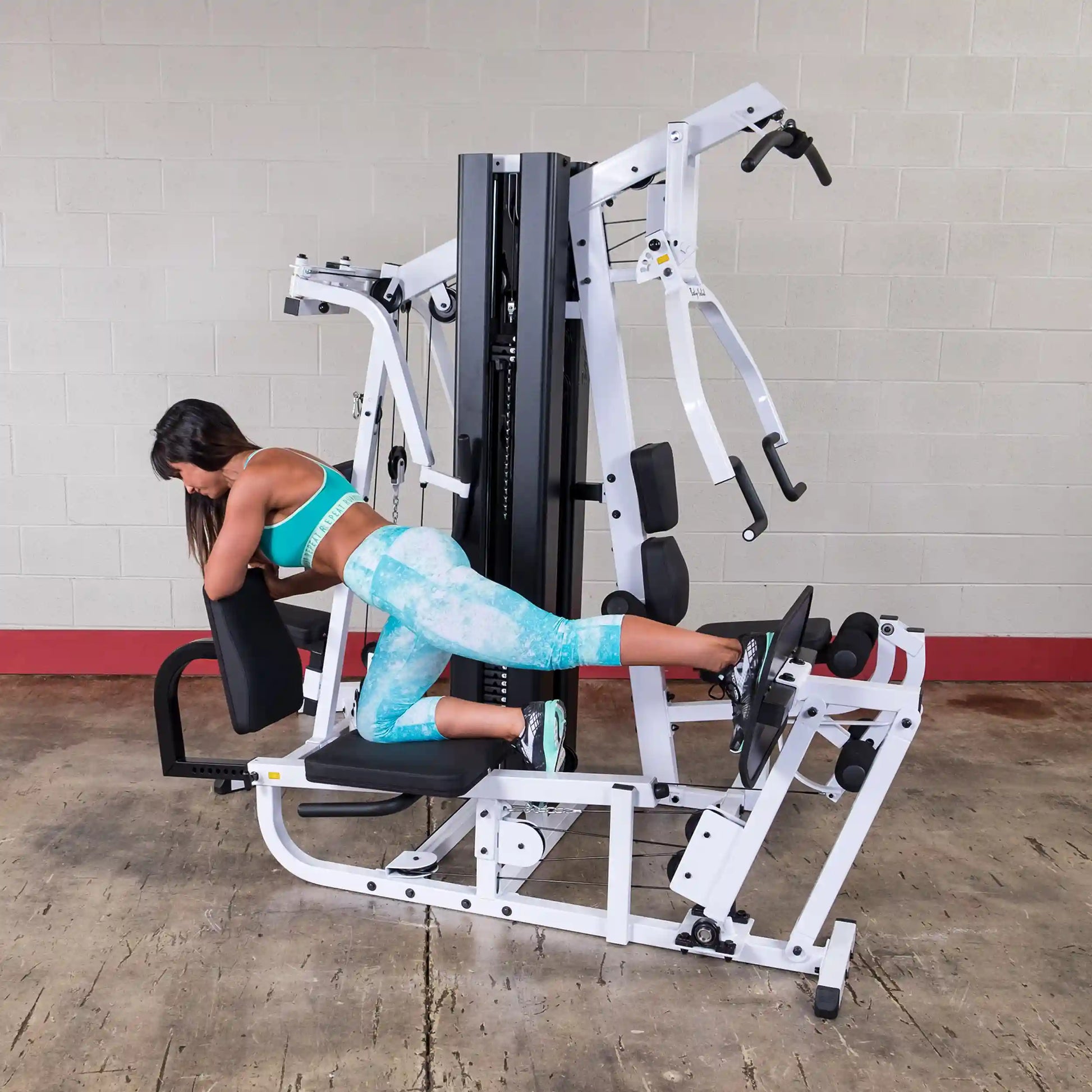 Woman in teal workout gear using a multi-gym leg press machine for exercise.