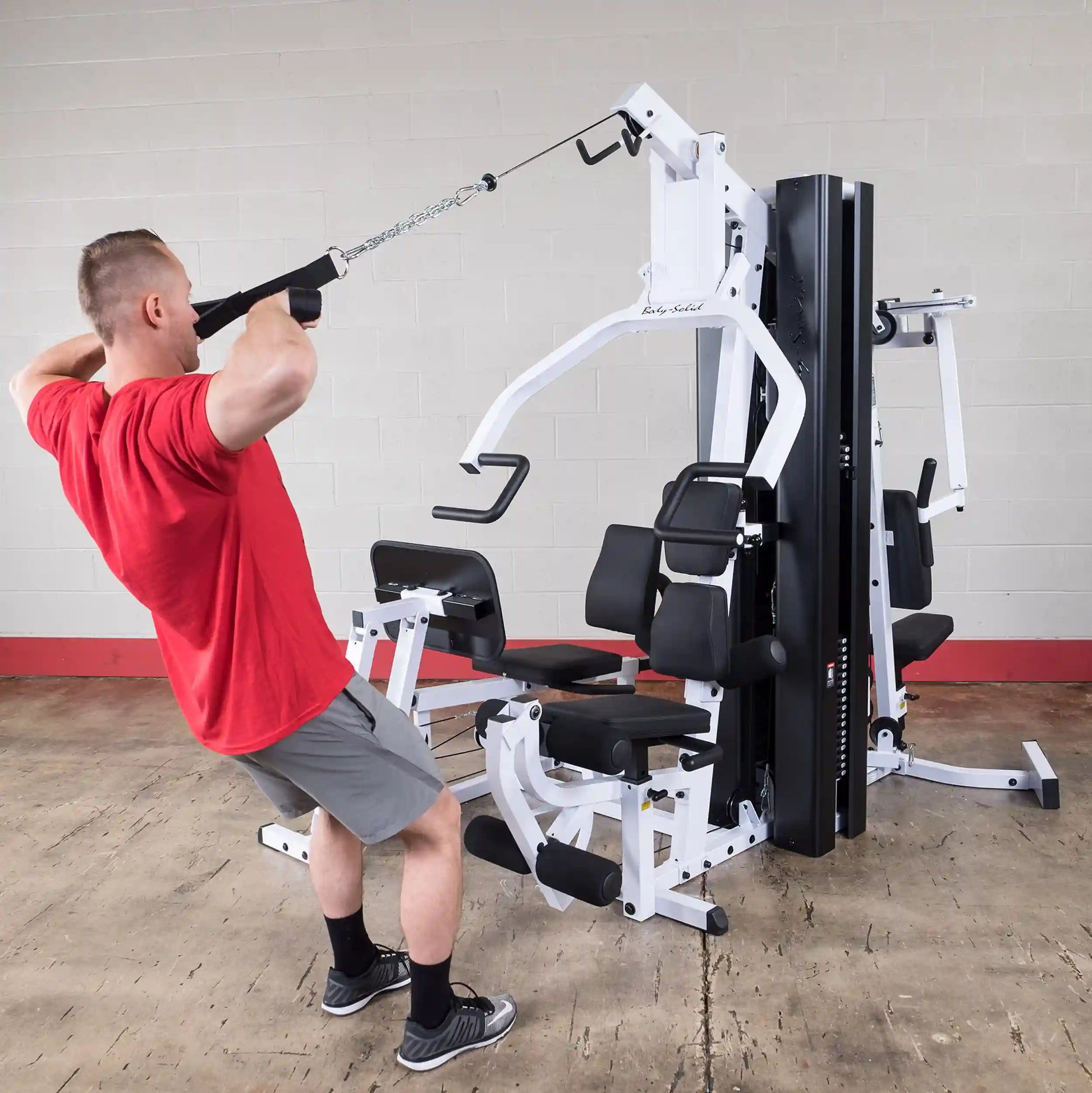 Man using Body-Solid home gym for tricep exercise, featuring black padded seats.