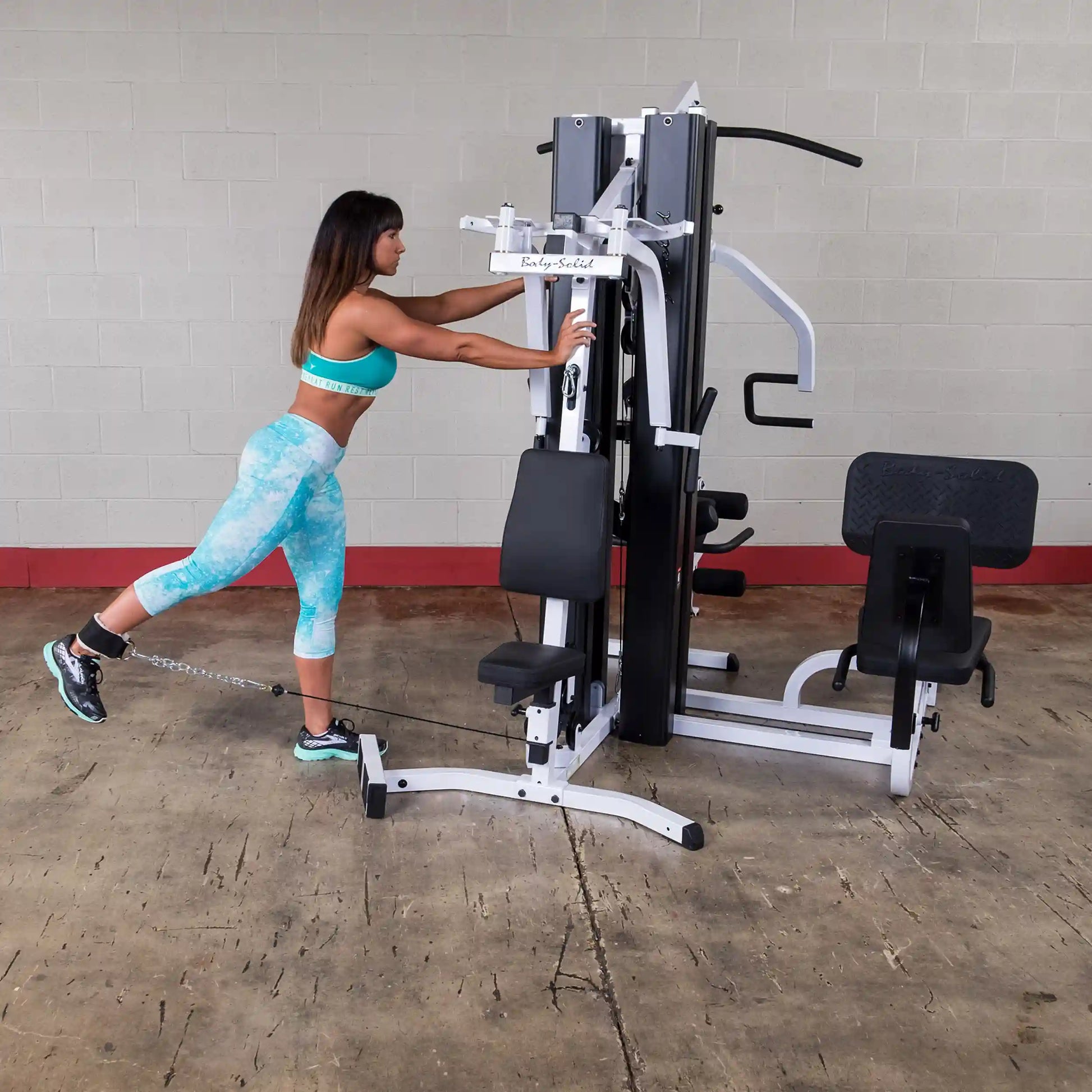 Woman exercising on Body-Solid home gym machine, wearing turquoise activewear.
