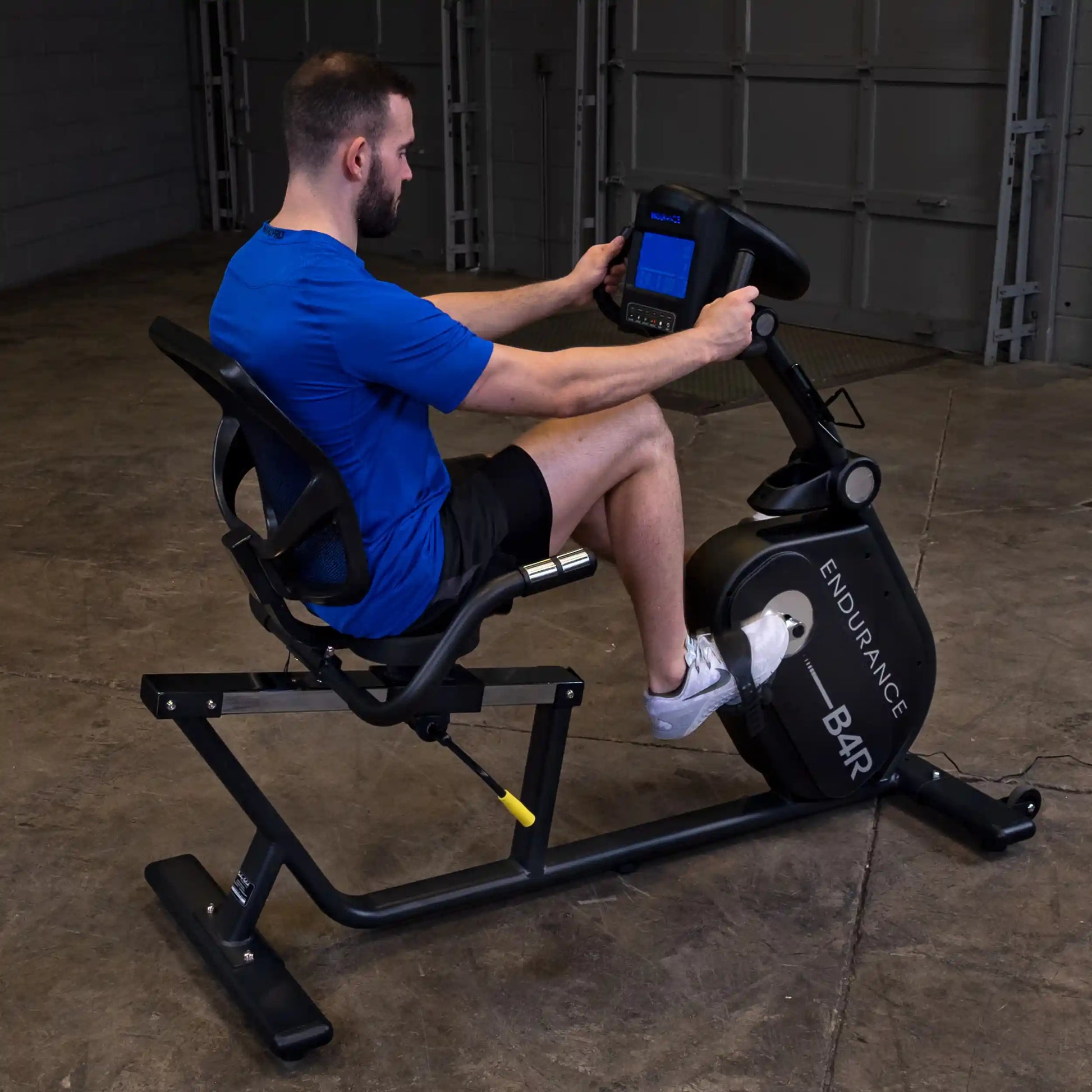 Man using Endurance B4R recumbent exercise bike in a garage gym.