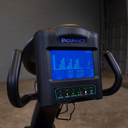 Endurance exercise bike with digital display showing workout metrics in a dimly lit gym.