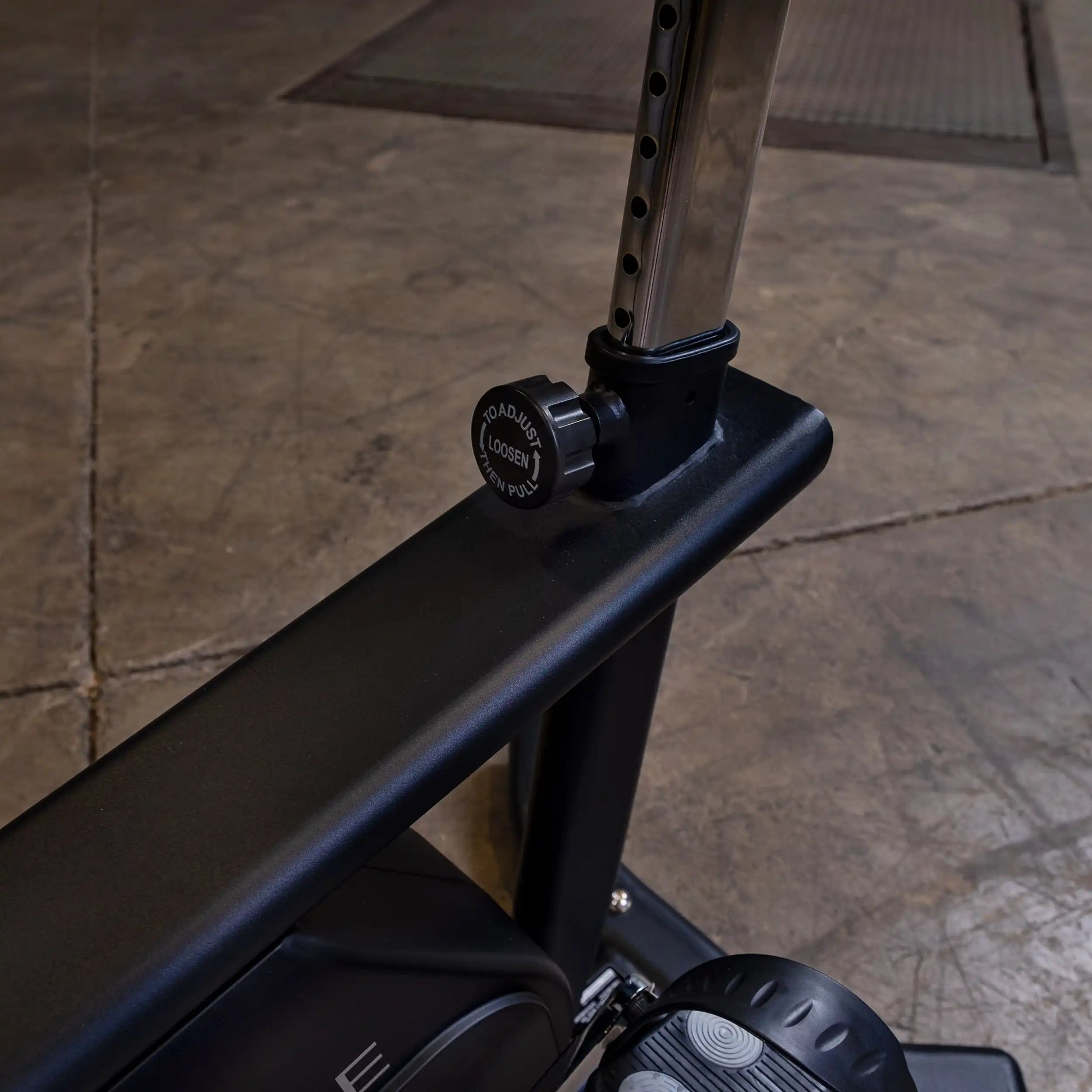 Adjustable black metal gym equipment with a knob for seat height.