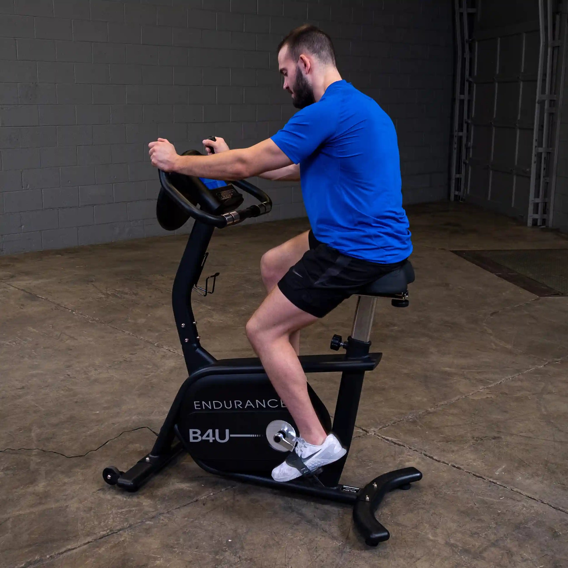 Man in blue shirt exercising on Endurance B4U stationary bike in a garage.