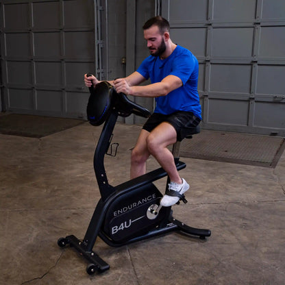 Man exercising on Endurance B4U stationary bike in a garage, wearing a blue shirt and black shorts.