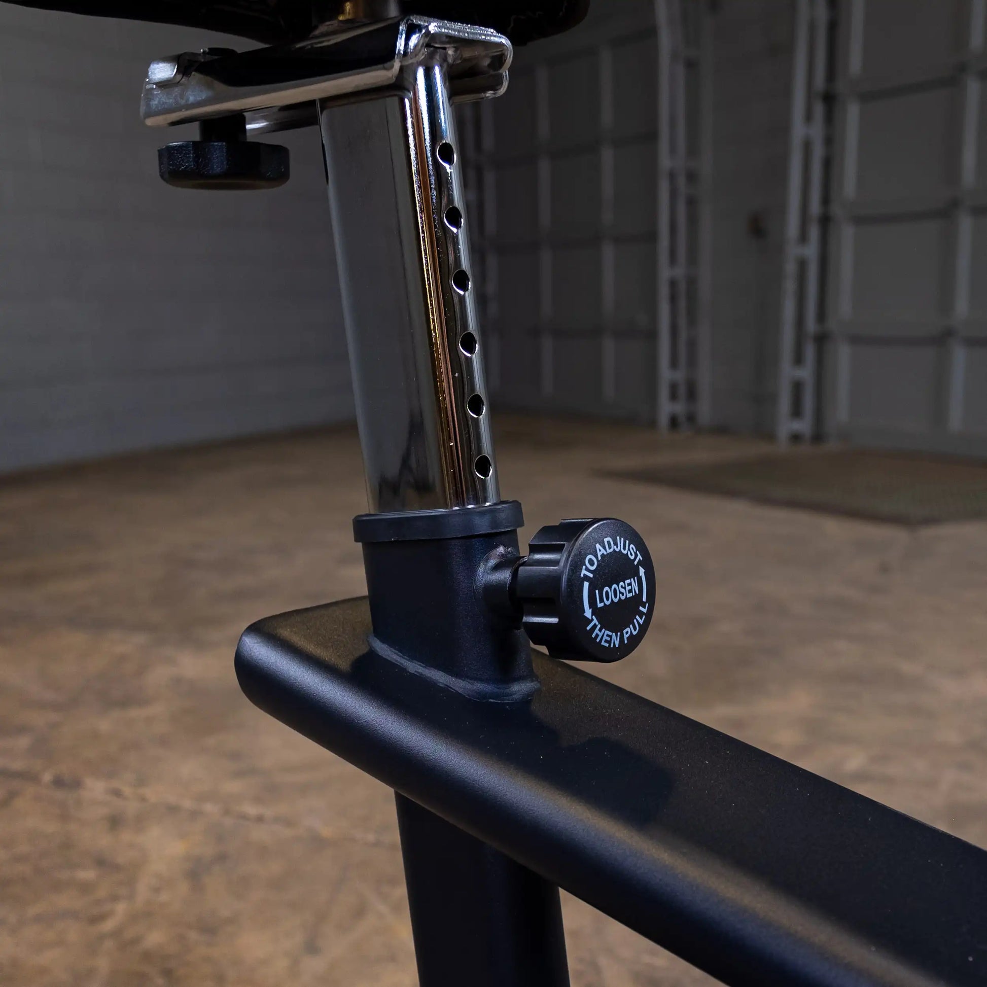 Adjustable weight bench seat with chrome support and black knob in a gym setting.