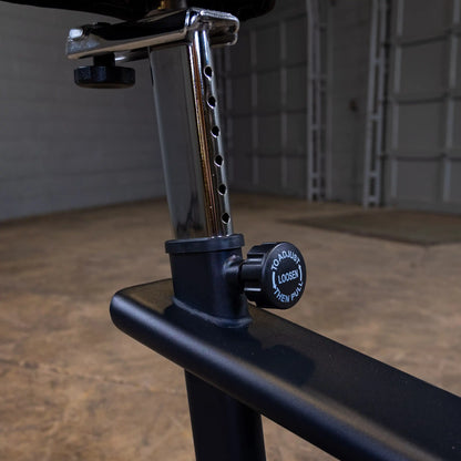 Adjustable weight bench seat with chrome support and black knob in a gym setting.