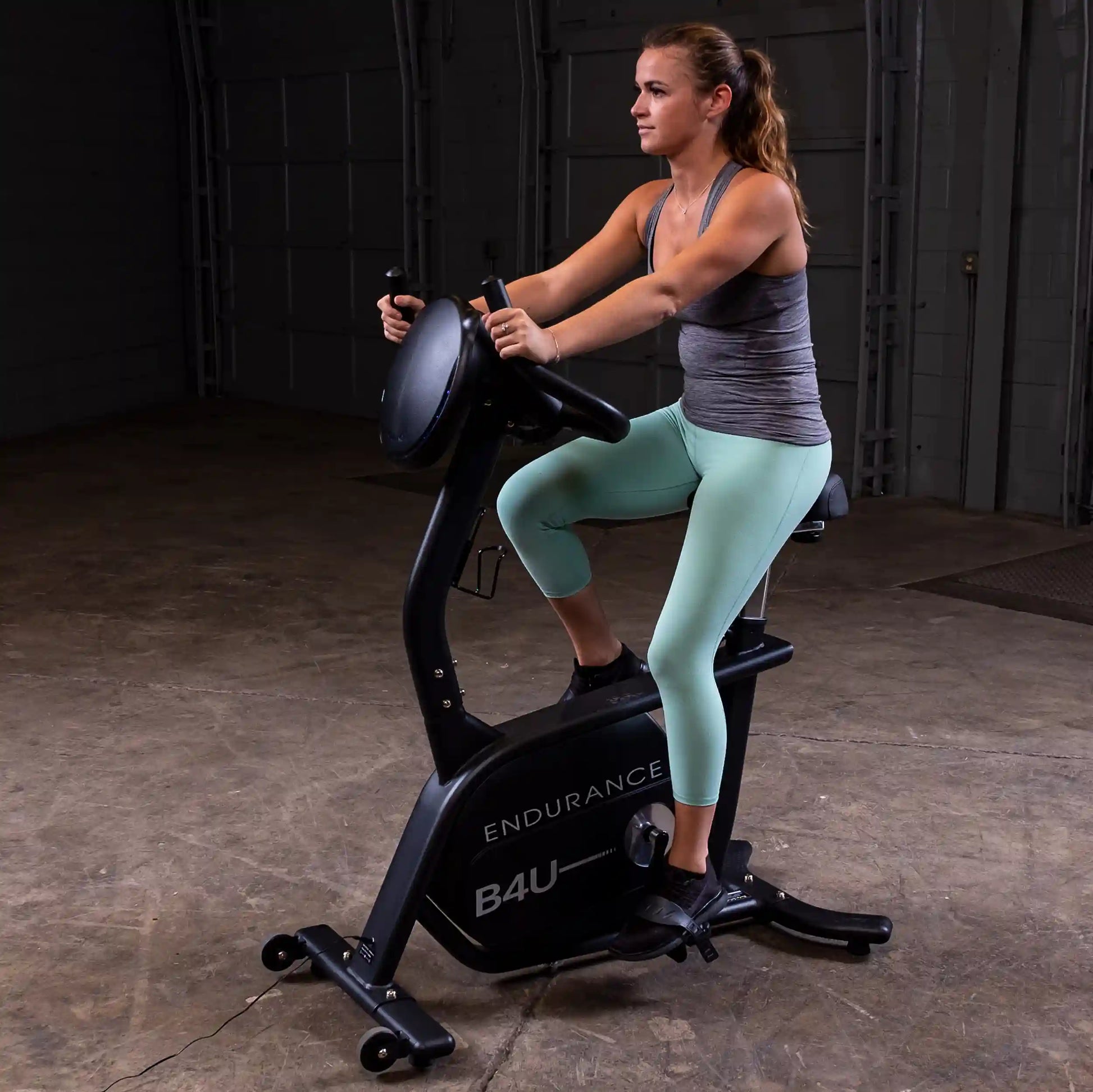 Woman exercising on Endurance B4U stationary bike in a dimly lit room.