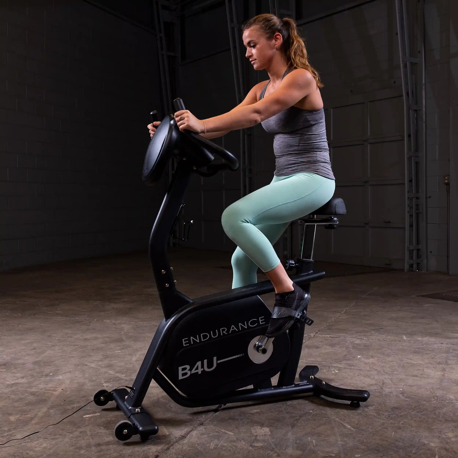 Woman exercising on Endurance B4U stationary bike in a dimly lit gym.