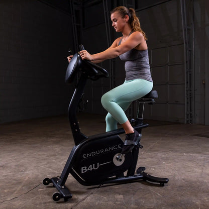Woman exercising on Endurance B4U stationary bike in a dimly lit gym.