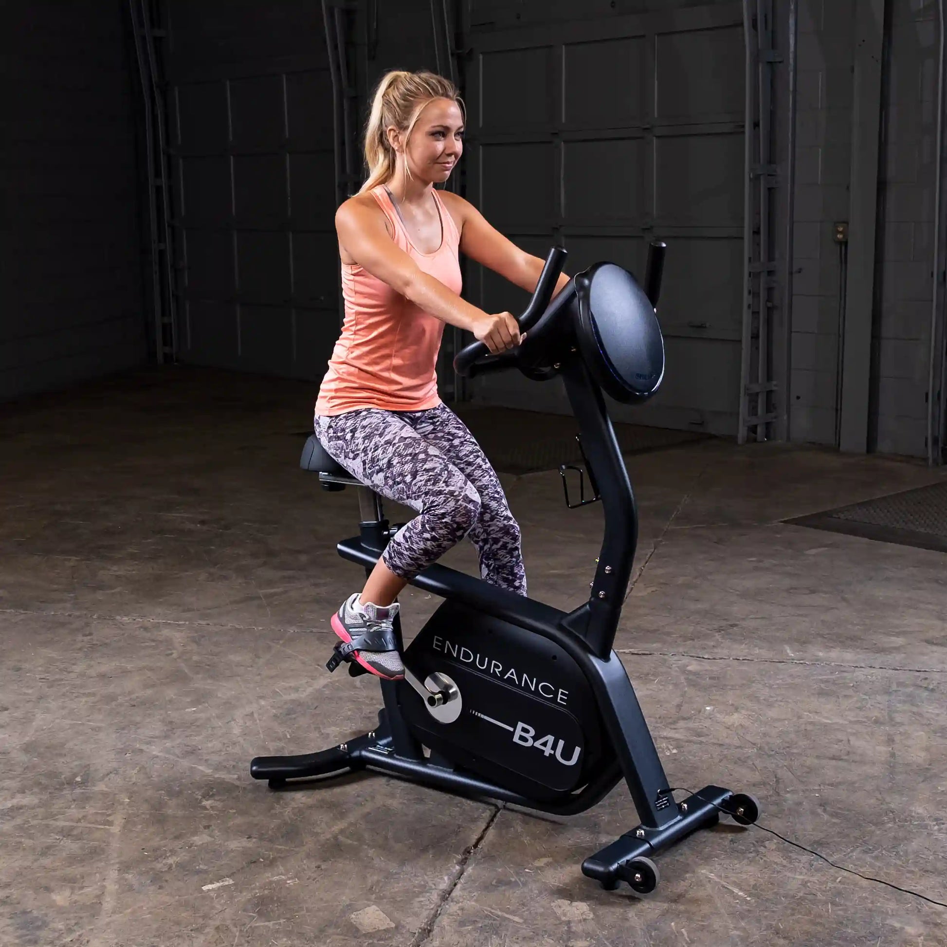 Woman exercising on Endurance B4U stationary bike in a garage, wearing patterned leggings.