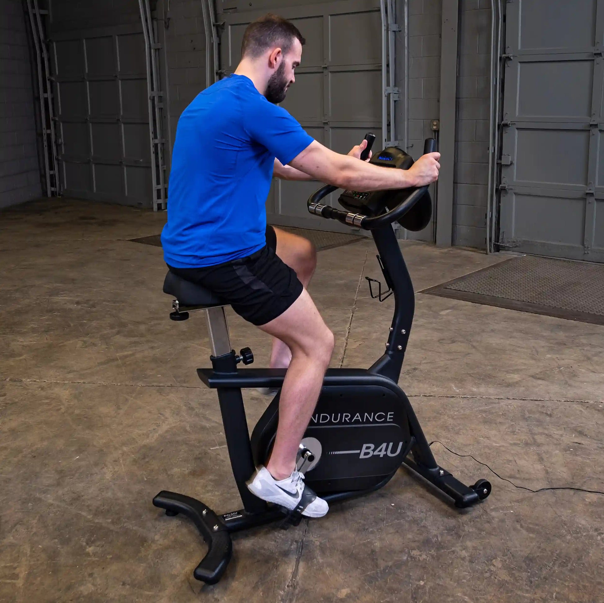 Man exercising on Endurance B4U stationary bike in blue shirt and black shorts.