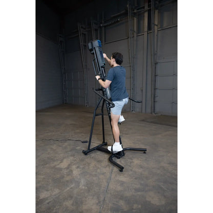 Man using END RANGER vertical climber in a warehouse, wearing gray shorts and black shirt.