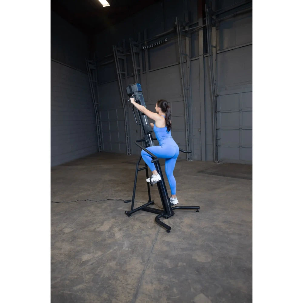 Woman in blue outfit using a MaxiClimber vertical climber in a warehouse gym.