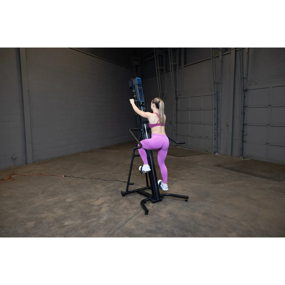 Woman in pink leggings using a vertical climber machine in a warehouse gym.