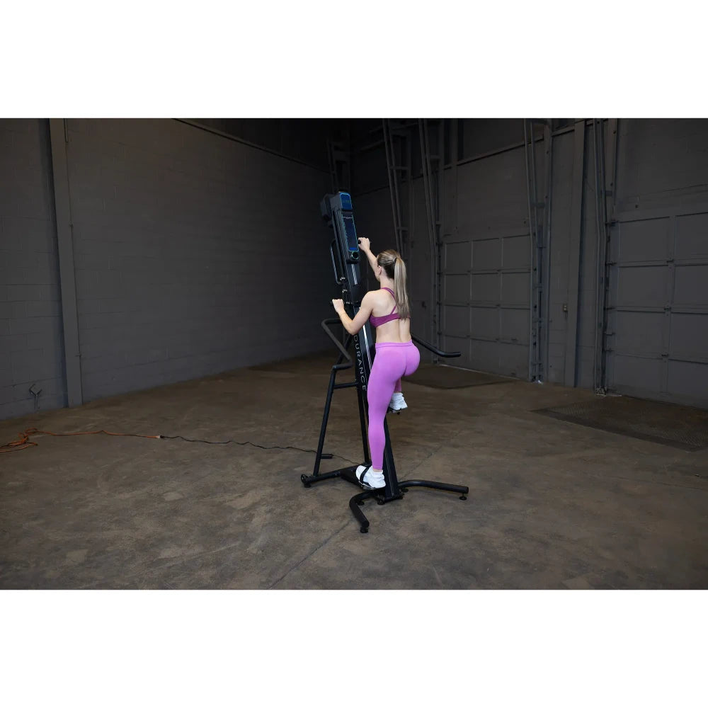 Woman in pink leggings using a black vertical climber machine in a large industrial gym.