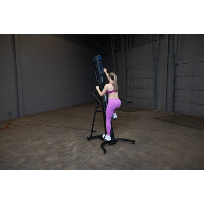 Woman in pink leggings using a black vertical climber machine in a large industrial gym.