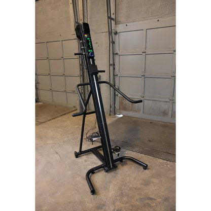 Vertical climber exercise machine in black with digital display in a garage setting.