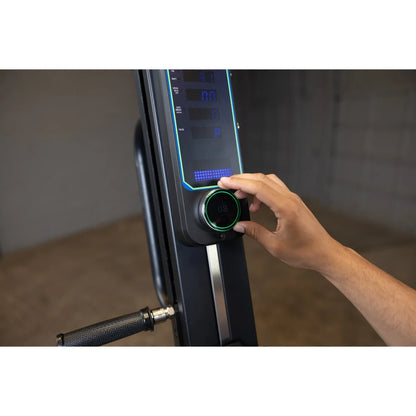 Adjusting resistance on a black rowing machine's digital display with a control knob.