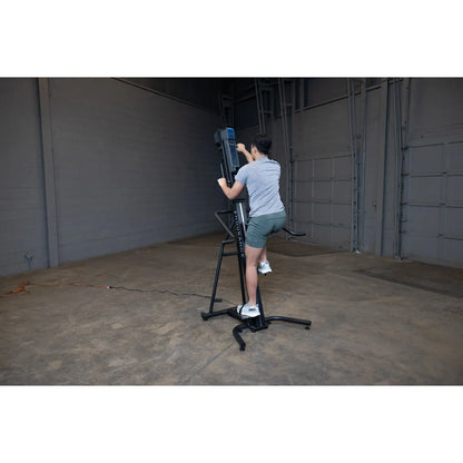 Person using a black vertical climbing machine for exercise in a gym.