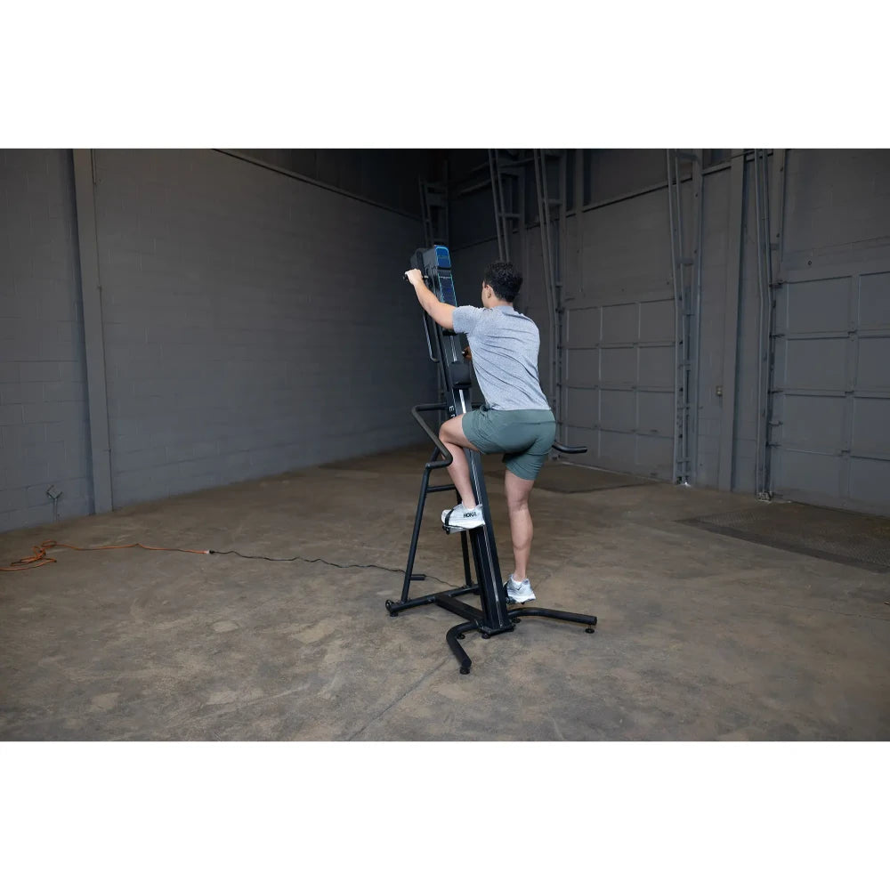 Person using a black vertical climber machine in a spacious industrial gym.