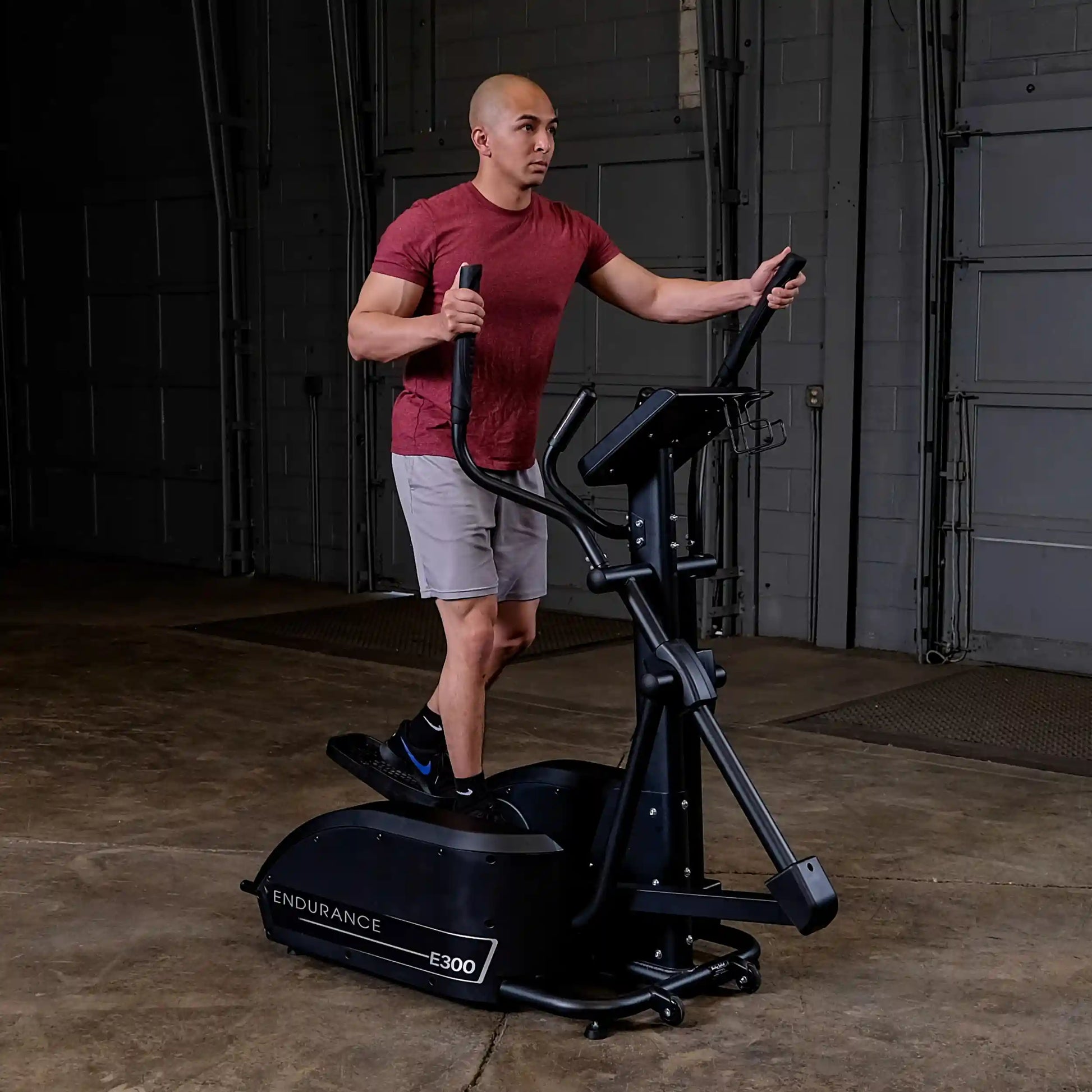 Man exercising on black Endurance E300 elliptical trainer in garage.
