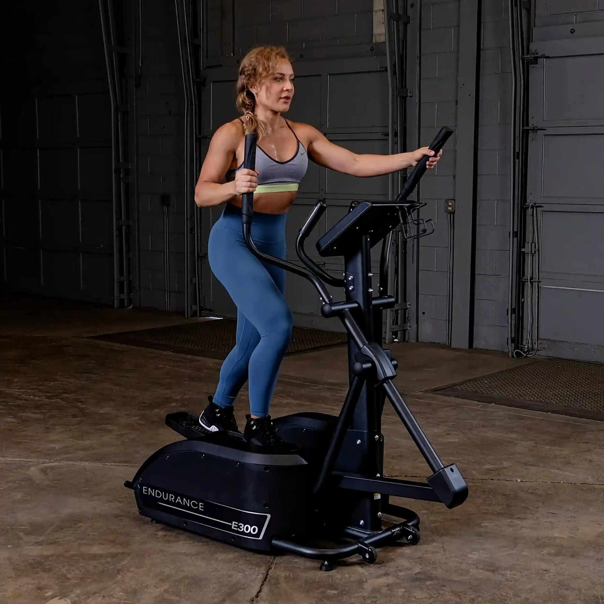 Woman using Endurance E300 elliptical in a gym wearing blue leggings.