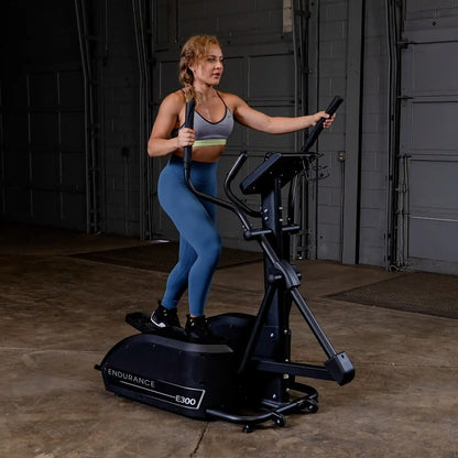 Woman using Endurance E300 elliptical in a gym wearing blue leggings.