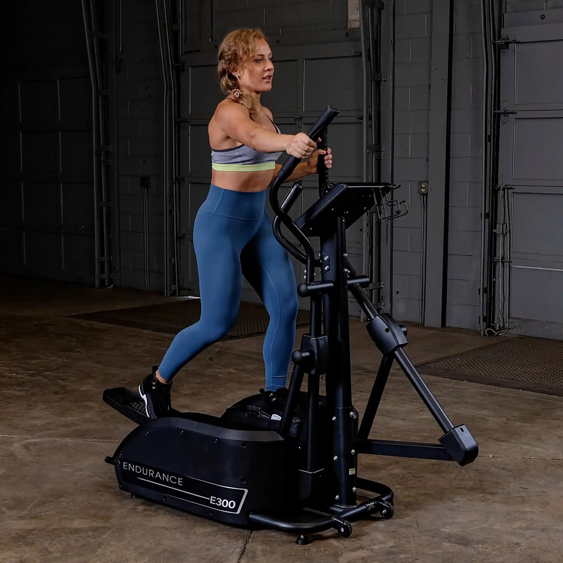 Woman exercising on Endurance E300 elliptical in a gym, wearing blue leggings.