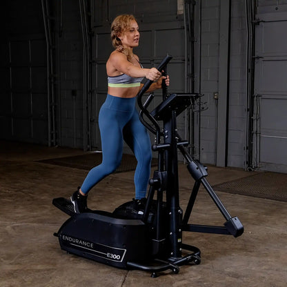 Woman exercising on Endurance E300 elliptical in a gym, wearing blue leggings.