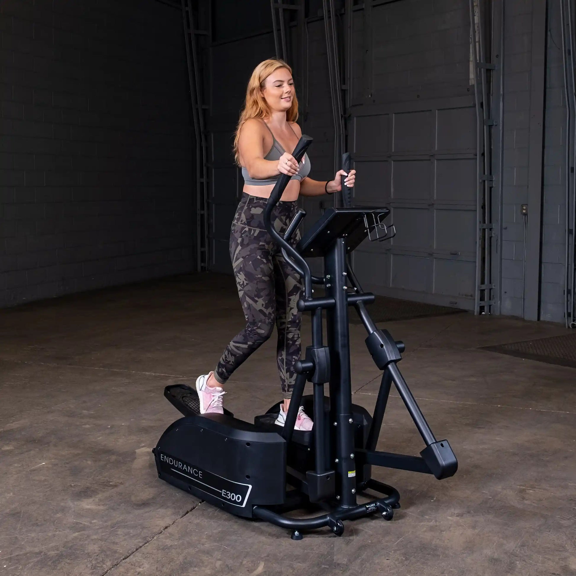Woman exercising on Endurance E300 elliptical in a dimly lit room.