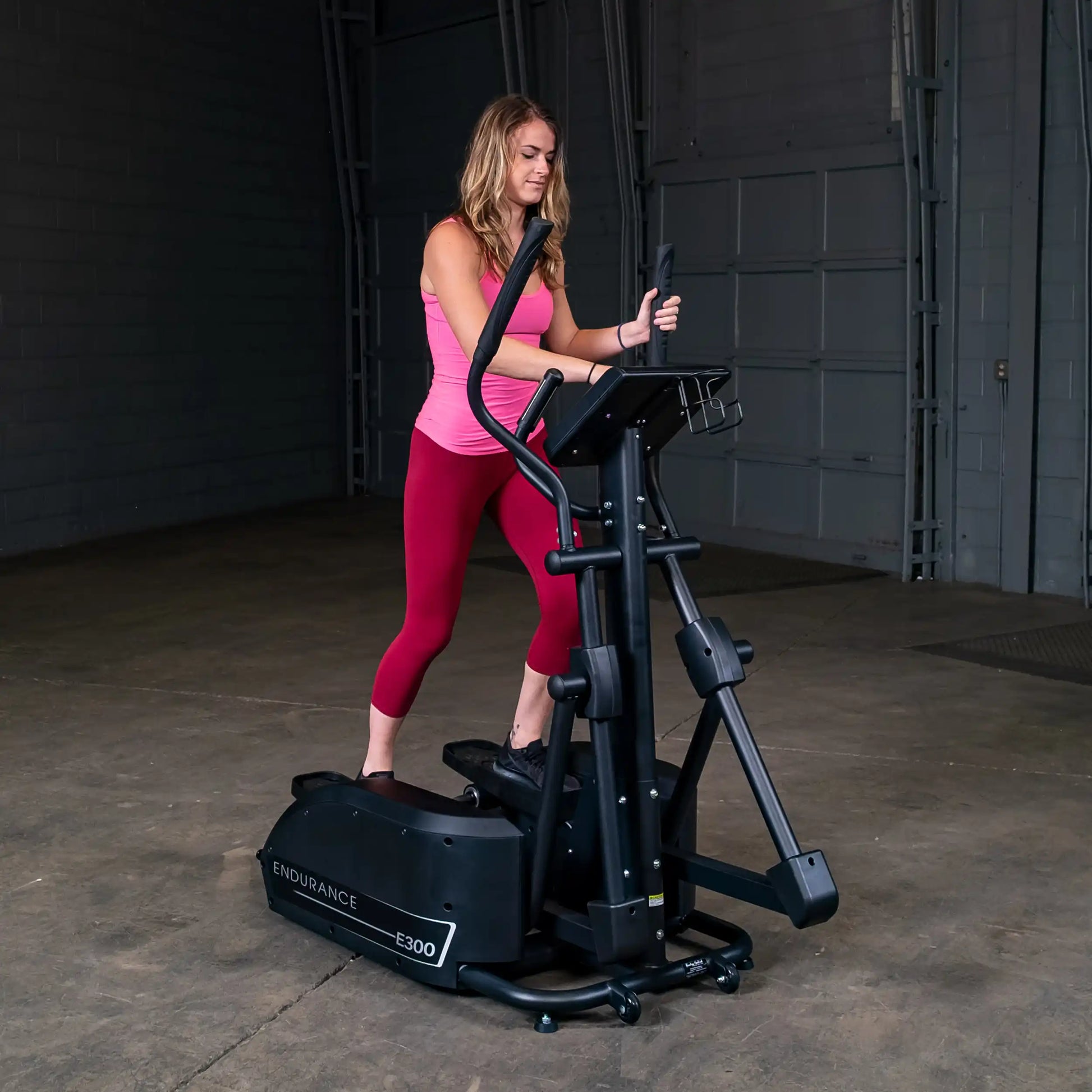 Woman using Endurance E300 elliptical trainer in a warehouse setting.
