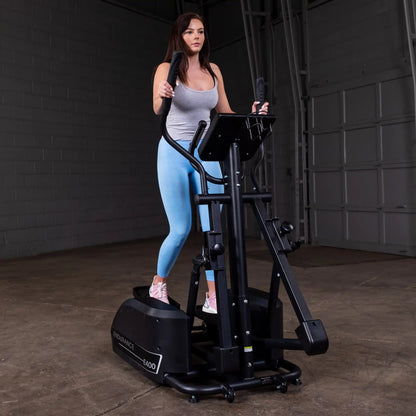 Woman using Endurance E400 elliptical trainer in a gym, wearing blue leggings and pink sneakers.