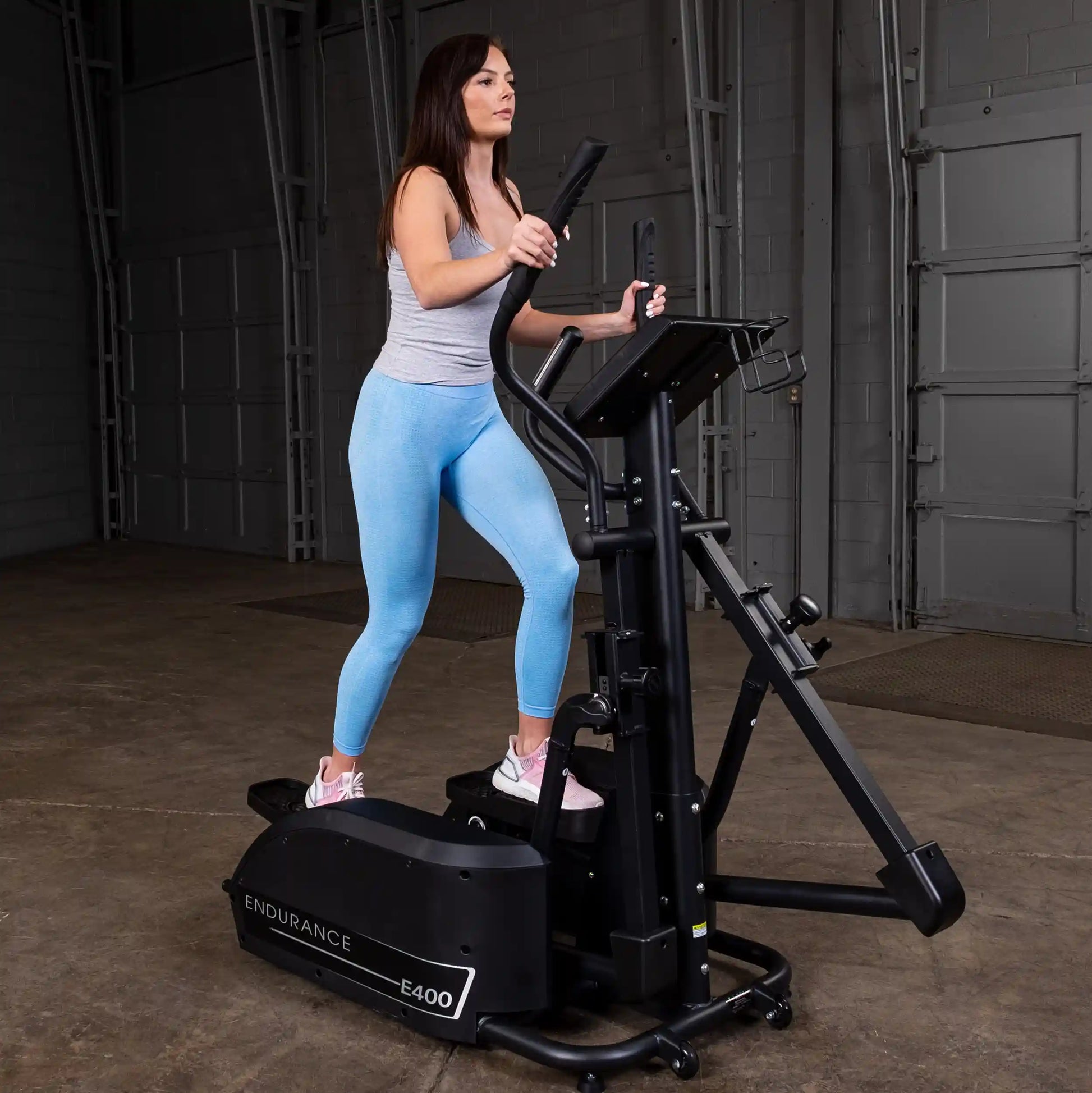 Woman exercising on Endurance E400 elliptical trainer in a gym wearing blue leggings.