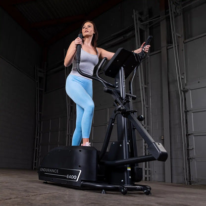 Woman exercising on Endurance E400 elliptical in a gym, wearing blue leggings and a gray top.