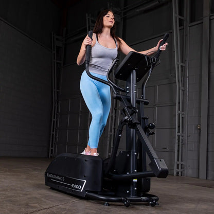 Woman using Endurance E400 elliptical machine in a gym, wearing blue leggings and a gray tank top.