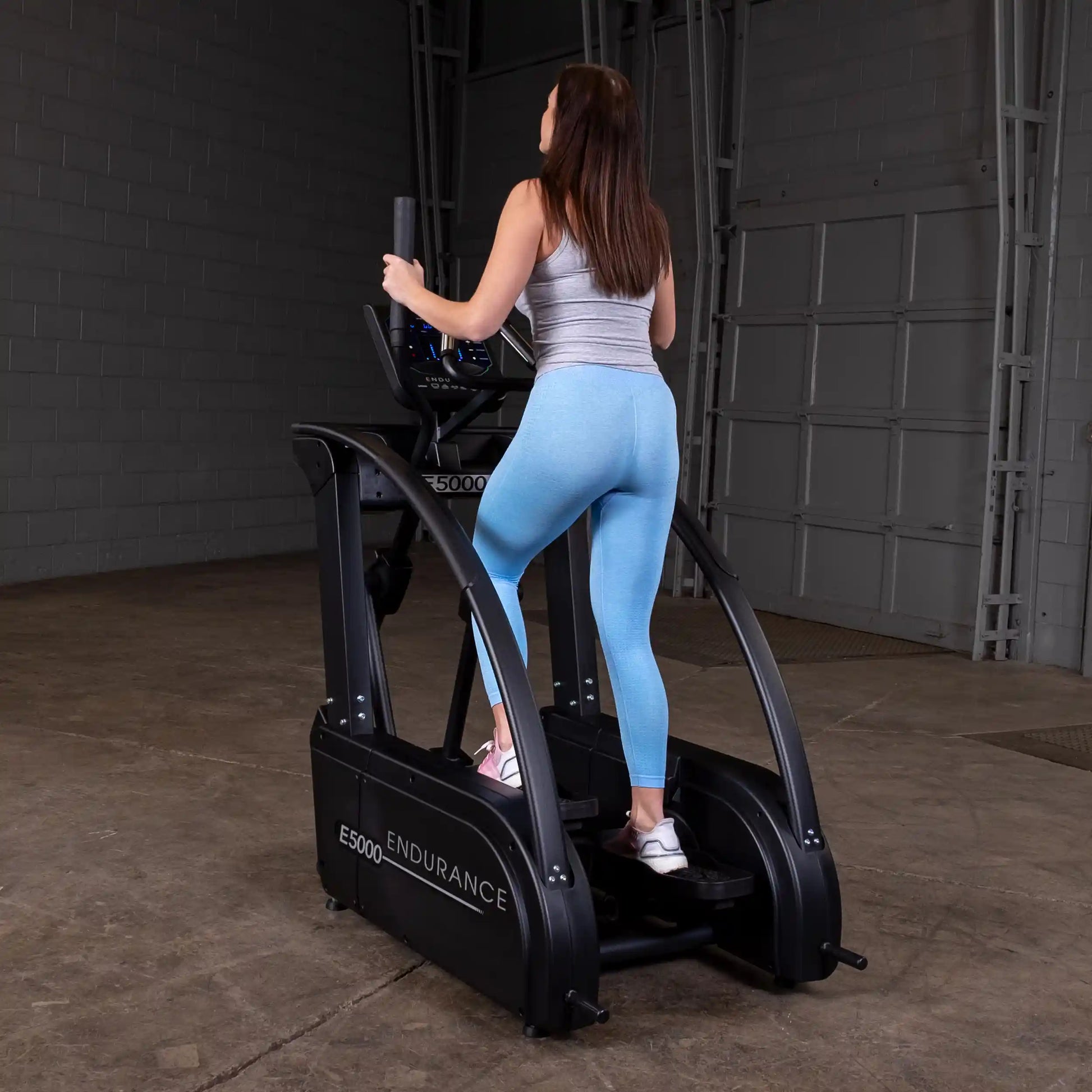 Woman using Endurance E5000 step machine in blue leggings for fitness.