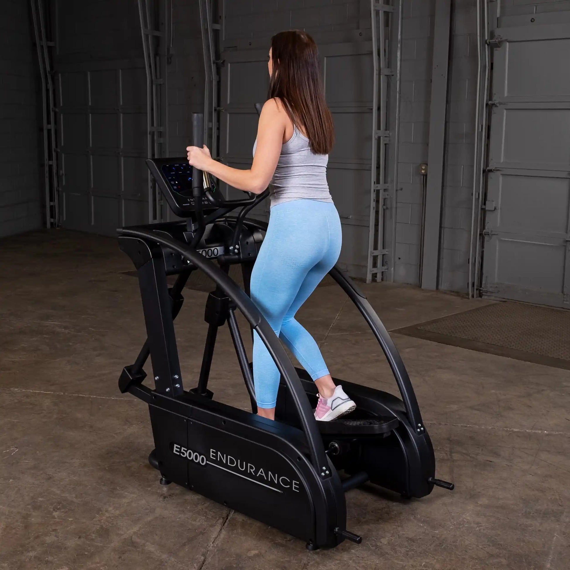 Woman using Endurance E5000 elliptical in a gray tank and blue leggings.