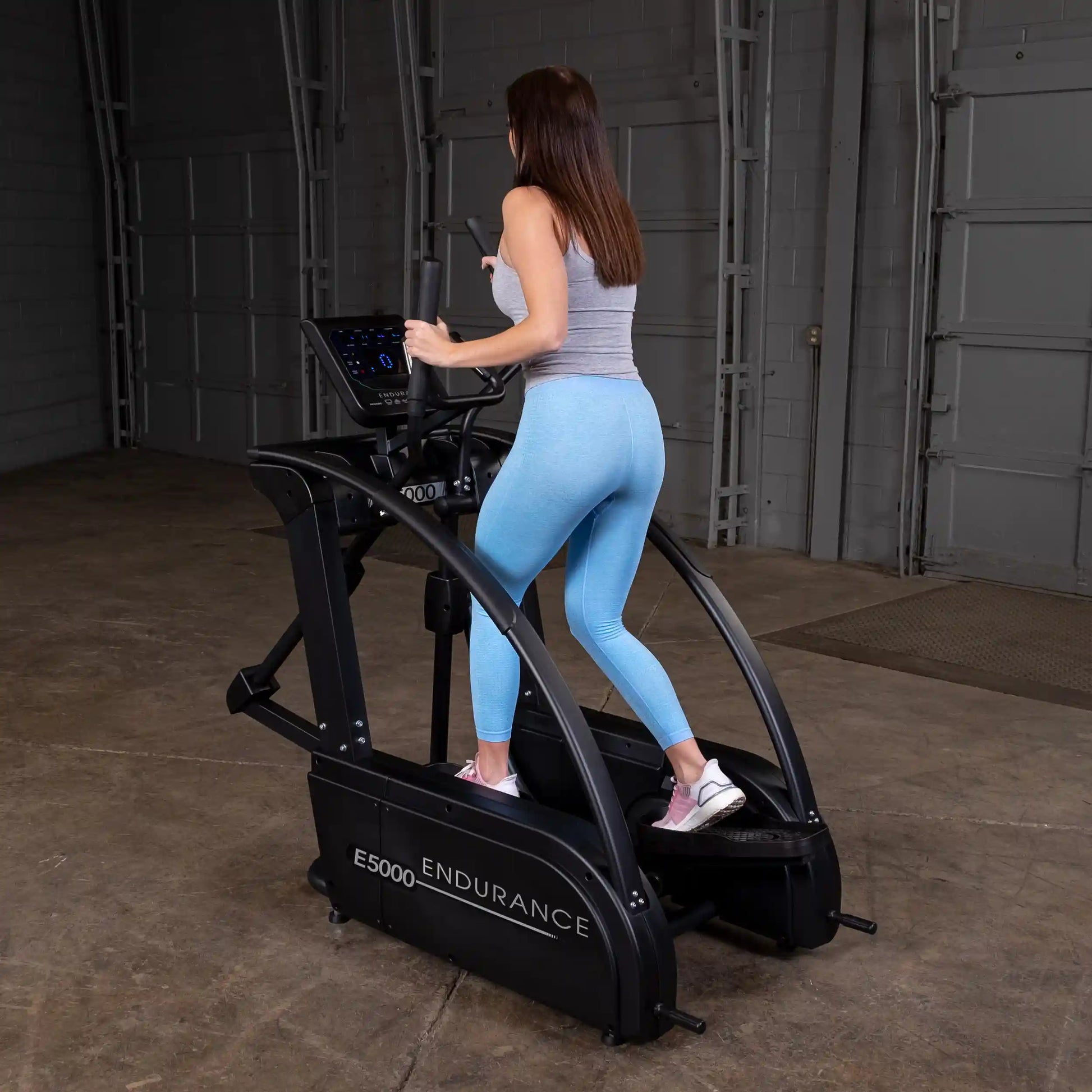Woman exercising on Endurance E5000 elliptical trainer in blue leggings.