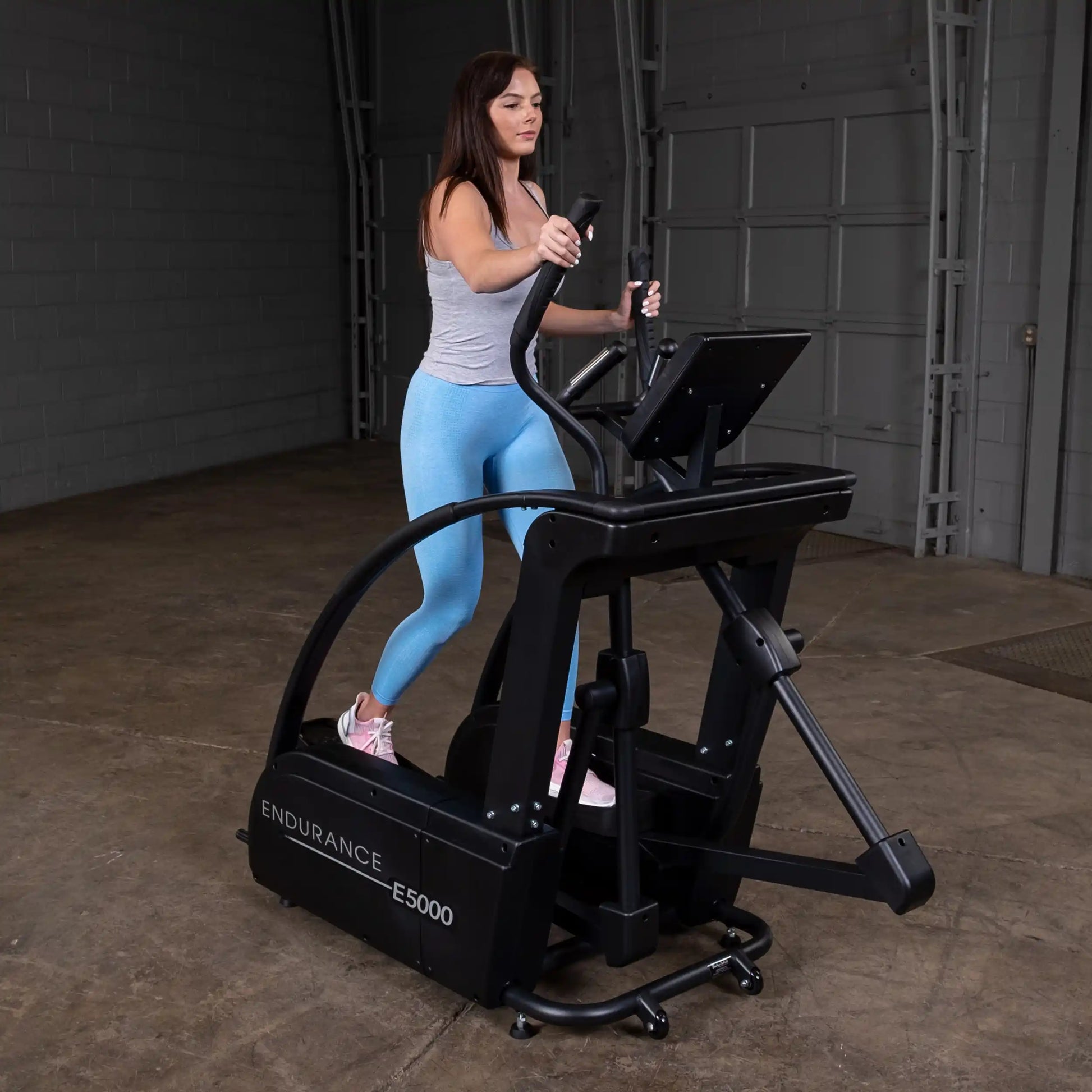 Woman exercising on Endurance E5000 elliptical trainer in a gray top and blue leggings.