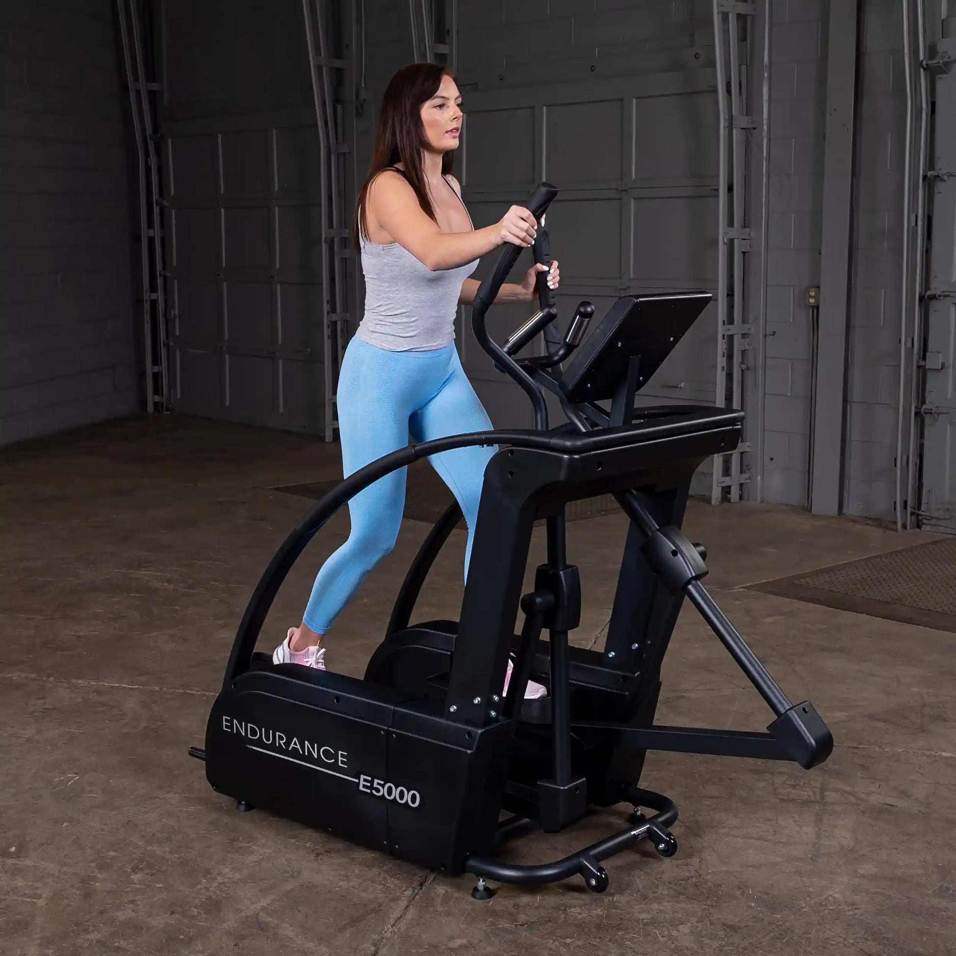 Woman exercising on Endurance E5000 elliptical trainer in a gray tank top and blue leggings.